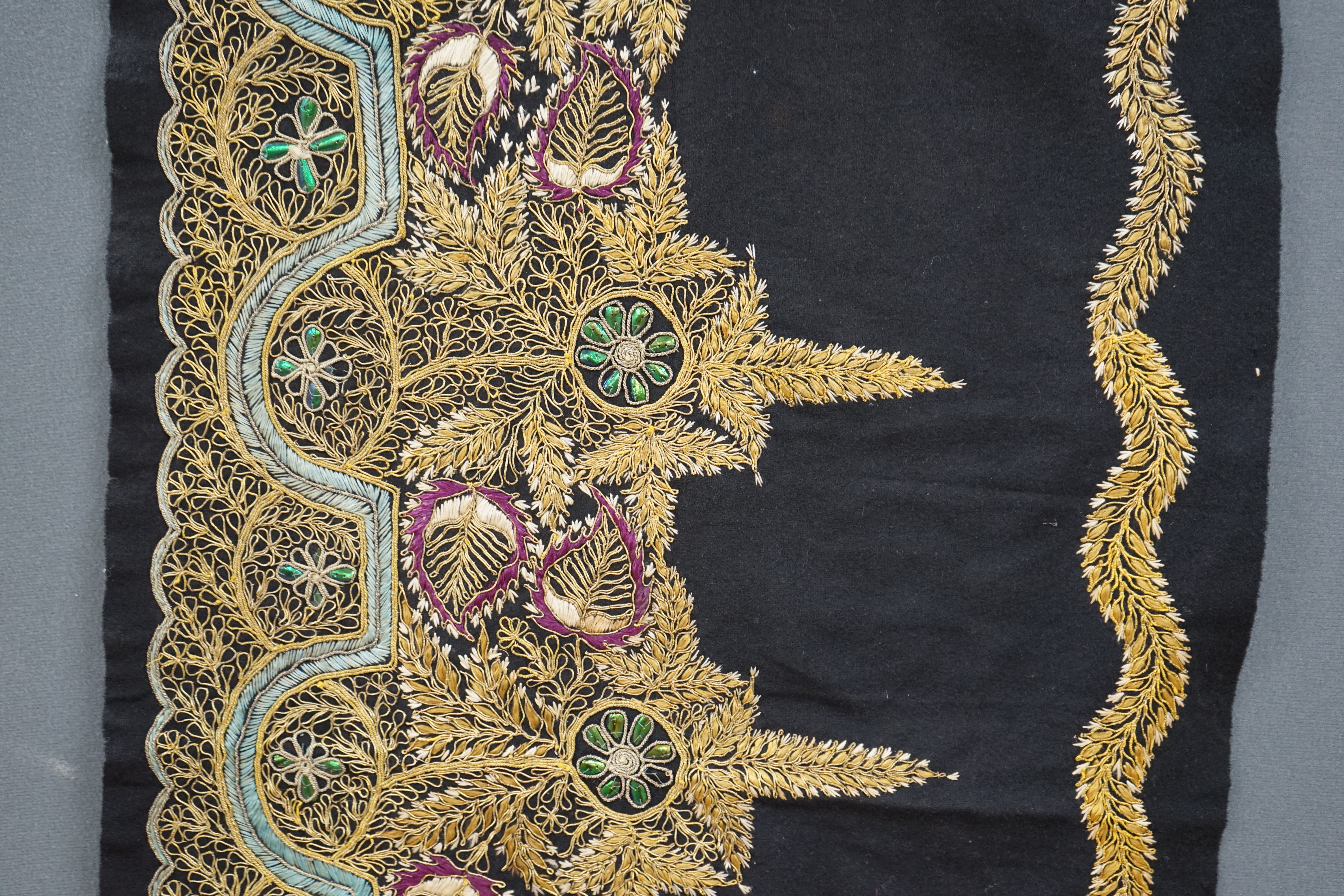 An Indian black felt panel embroidered with mostly gold thread, some coloured silks and beetle wing ornamentation, possibly a border to a larger panel, 256cm long. Condition - good